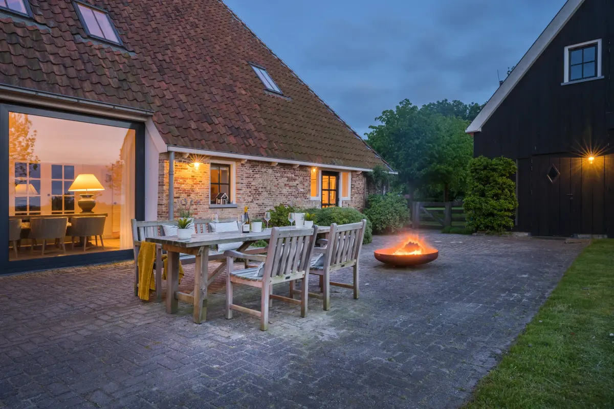 Een terras met vuurschaal en wijnglazen bij een Friese kop-hals-rompboerderij, in het laatste licht