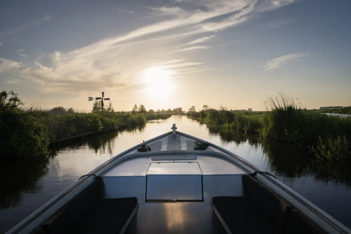 Varen over een smalle Friese vaart, met een molen aan de horizon in de late zon