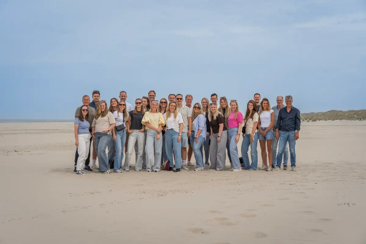 Het team van Wente op het strand, in een brede rij op het zand met de zee erachter